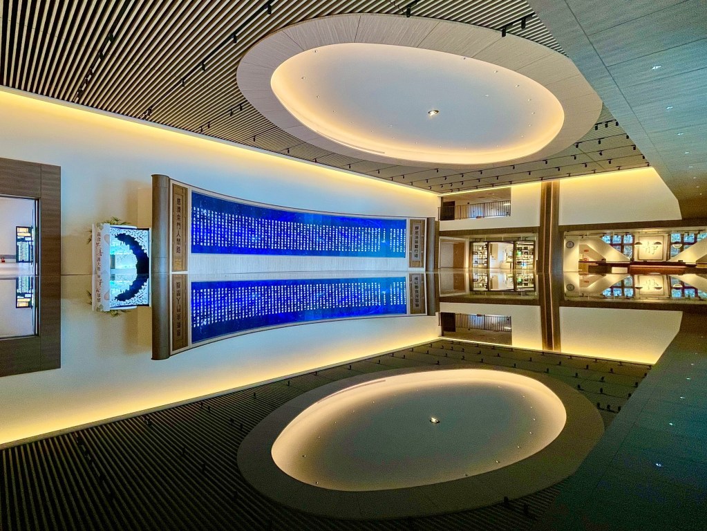 現代建築內部，顯示藍色燈光的弧形牆面，兩側有展示區，中央有圓形天花板，整體設計簡潔雅致。